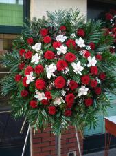 Wieniec pogrzebowy z żywych kwiatów, kształt okrągły, róże pąsowe, storczyki białe (Cymbidium), liście Chico, liście Salal, podkład jodłowy, zieleń dekoracyjna.