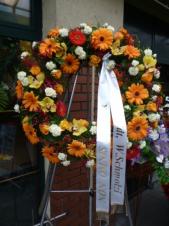 Wieniec pogrzebowy z żywych kwiatów, kształt okrągły średnica ok. 90cm (wieniec rzymski), róże herbaciane i kremowe, gerbera żółta, storczyki złote (Cymbidium), chryzantema zielona (Santini), goździk gałązkowy biały, zieleń dekoracyjna, szarfa satynowa 7cm (+20 zł).