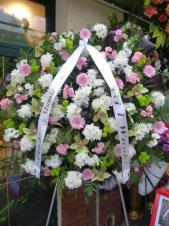 Wieniec pogrzebowy z kwiatów żywych, kształt okrągły, gerbera różowa, chryzantema gałązkowa biała, goździk gałązkowy różowy, storczyk zielony (Cymbidium), chryzantema gałązkowa zielona Santini, eustoma biała, podkład jodłowy, zieleń dekoracyjna.