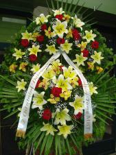 Wieniec z żywych kwiatów, wielkość: bardzo duży, lilie kremowe (Conca D'Or), storczyki złote (Cymbidium), róże pąsowe, liść palmy, podkład jodłowy, zieleń dekoracyjna, szarfa satynowa 7cm, druk komputerowy.