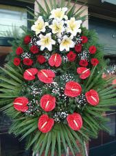 Wieniec z żywych kwiatów, wielkość: średni, lilie białe (Casablanca), storczyki złote (Cymbidium), anthurium czerwone, liść palmy, podkład jodłowy, zieleń dekoracyjna.