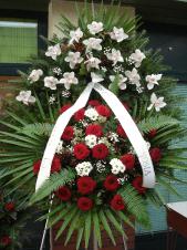 Wieniec z żywych kwiatów, wielkość: duży, storczyki białe (Cymbidium), róże pąsowe, chryzantemy białe (Bacardi), liście palmy, podkład jodłowy, zieleń dekoracyjna.