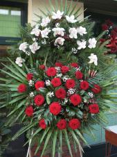 Wieniec pogrzebowy z żywych kwiatów, wielkość: średni, storczyki białe (Cymbidium), róże pąsowe, liście palmy, podkład jodłowy, zieleń dekoracyjna.