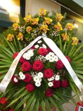 Wieniec z żywych kwiatów, wielkość: średni, storczyki złote (Cymbidium), róże czerwone, chryzantemy białe, liść palmy, podkład jodłowy, szarfa plastikowa, druk komputerowy.