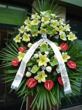 Wieniec pogrzebowy z żywych kwiatów, wielkość: bardzo duży, lilie kremowe (Conca D'or), anthurium czerwone i zielone, liście palmy, podkład jodłowy, zieleń dekoracyjna, szarfa satynowa 10cm, druk komputerowy.